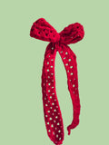 Red knitted headband with a bow held by a hand against a white background